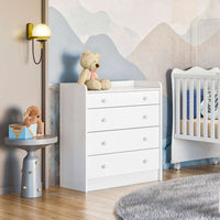 A white baby changing station with four drawers, placed next to a crib in a nursery room. The changing station has a smooth surface with knobs on the drawers and a plush toy rests on top.